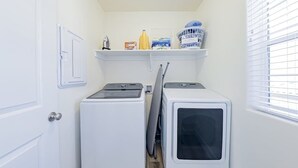 A laundry room with two white washers and dryers, a shelf with laundry supplies, and a door with a light switch. - 5BR townhouse with lazy river pool (Washington)