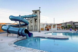 A swimming pool with a water slide and a building with arched windows in the background. - 5BR townhouse with lazy river pool (Washington)