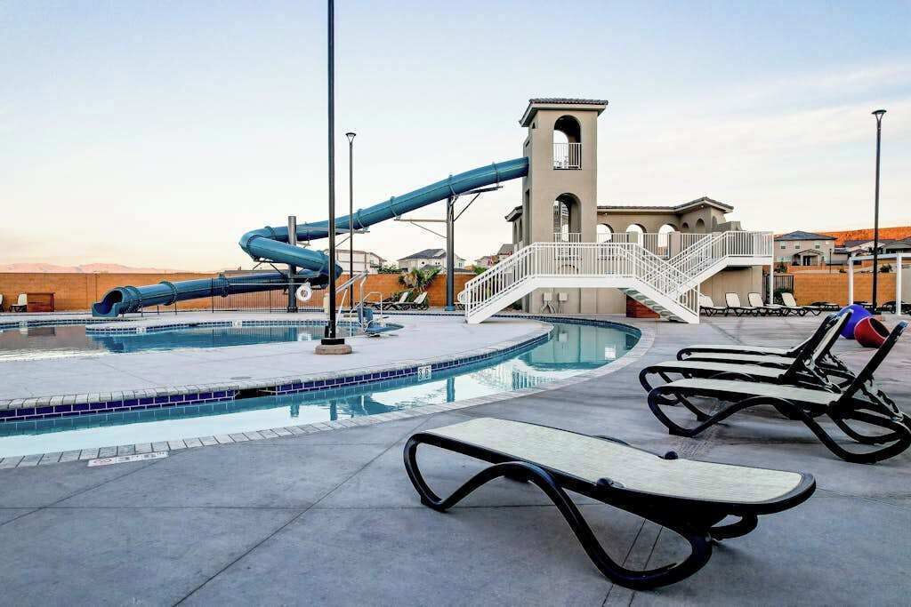 A swimming pool with a water slide, lounge chairs, and a small building with a balcony.