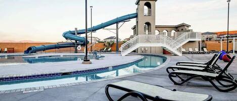 A swimming pool with a water slide, lounge chairs, and a small building with a balcony.