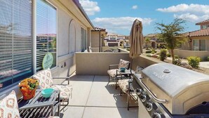 Eine Terrasse mit Grill, Sitzgelegenheiten im Freien und Blick auf angrenzende Häuser.