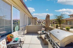 Eine Terrasse mit Grill, Sitzgelegenheiten im Freien und Blick auf angrenzende Häuser.