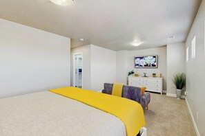 Ein Schlafzimmer mit einem großen Bett, einem Schminktisch, einem Fernseher und einer Zimmerpflanze.