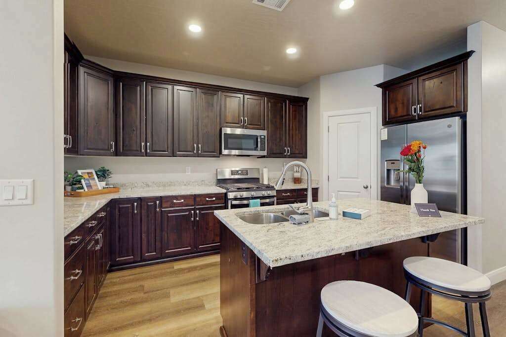 A modern kitchen with dark wood cabinets, stainless steel appliances, a granite countertop, and a built-in island with stools.
