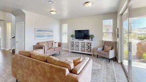 A spacious living room with a large sectional sofa, a television on a white console, and a view through a glass door. - 3BR townhouse with hot tub and heated pool (Washington)