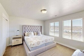 A bedroom with a tufted headboard, a bed with a floral bedspread, a nightstand, and large windows with a view. - 3BR townhouse with hot tub and heated pool (Washington)