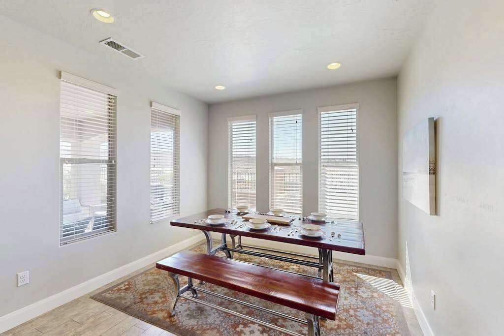 A dining area with a table set for four, a bench, and a patterned rug.