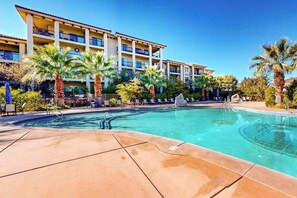 Ein Hotel mit Swimmingpool, Palmen und einem mehrstöckigen Gebäude mit Balkonen.