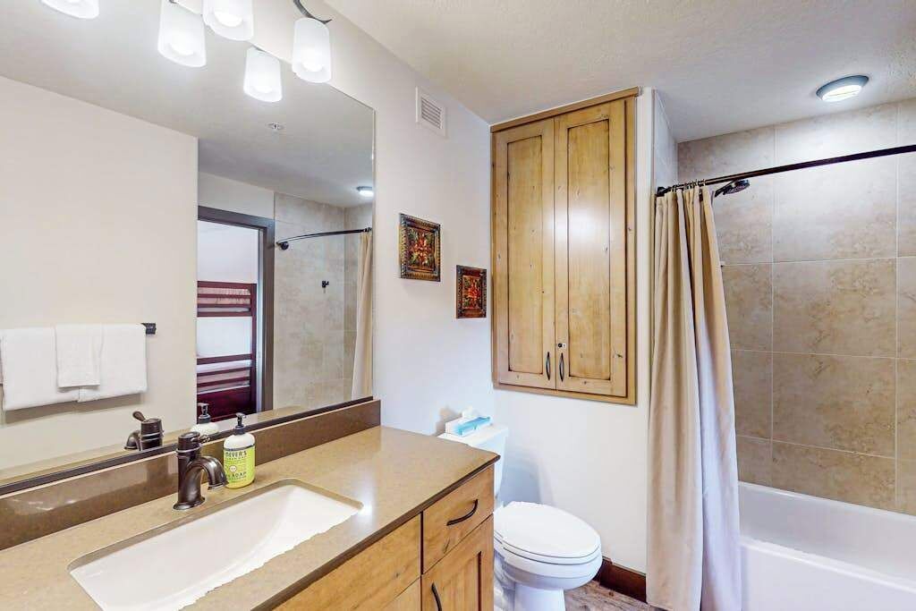 Un baño con lavamanos, espejo, armario, inodoro y cortina de ducha.