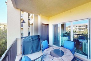 Ein Balkon mit Tisch und Stühlen, einem überdachten Grill und einer Schiebetür zu einer Terrasse.