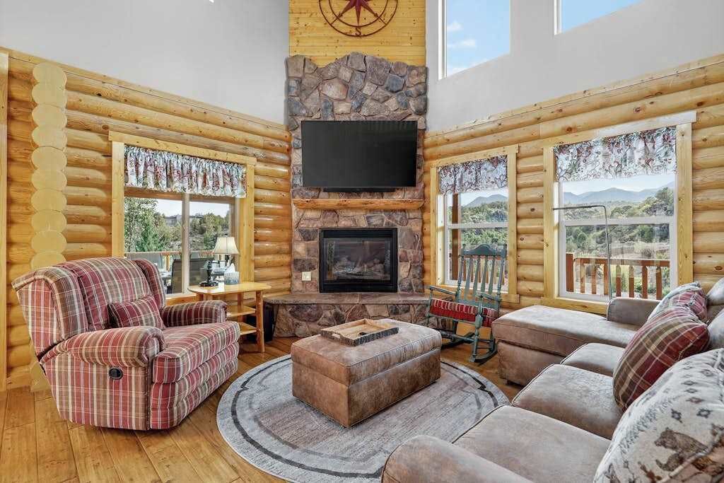 L’intérieur d’un chalet en rondins, avec une cheminée, un téléviseur et une vue sur l’extérieur.