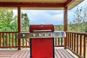 Ein roter Grill auf einer Terrasses mit Holzgeländern und Blick auf Bäume und Hügel.