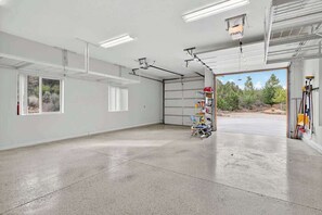 Eine geräumige Garage mit Betonboden, einer Werkbank mit Werkzeugen und einem großen Fenster mit Blick ins Freie.