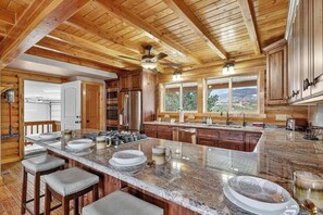 A spacious kitchen with wooden beams, a large island with bar stools, and a view of the outdoors. - 4BR home - wrap around porch, fire pit & hot tub (New Harmony)