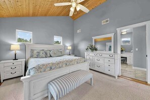 Ein Schlafzimmer mit Bett, Nachttischen, einem Schminktisch, einer Bank und einem Deckenventilator.