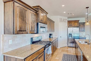 A kitchen with wooden cabinets, a stainless steel refrigerator, and a granite countertop. - 5BR spacious home with pool, hot tub, & foosball (Hurricane)