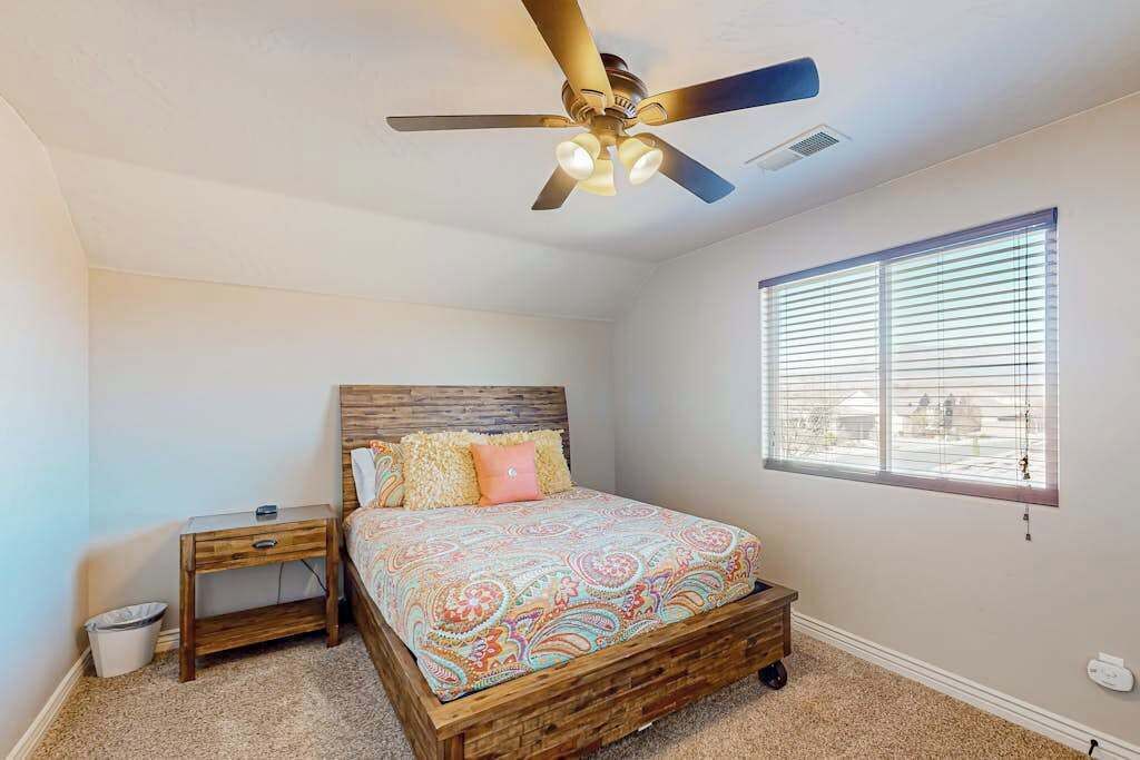 A bedroom with a bed, a nightstand, a ceiling fan, and a window with blinds.