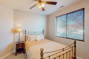 A bedroom with a bed, a nightstand, a lamp, a ceiling fan, and a window with blinds. - 5BR spacious home with pool, hot tub, & foosball (Hurricane)