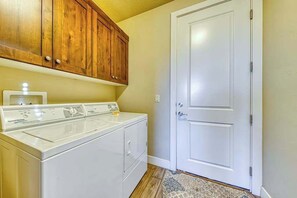 A laundry area with a front-loading washer and dryer, wooden cabinets above, and a white door to the right. - Spacious 5BR Mountainview Paradise Village (Santa Clara)