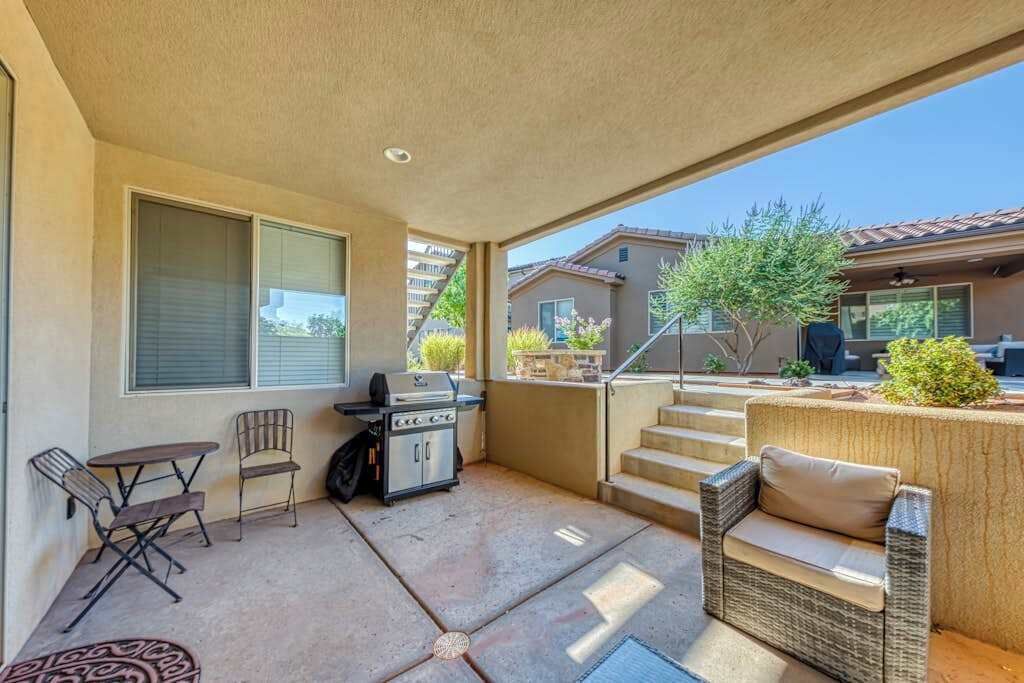 A covered patio with a grill, outdoor furniture, and a view of neighboring buildings.