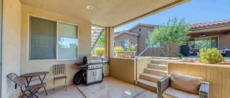 A covered patio with a grill, outdoor furniture, and a view of neighboring buildings.