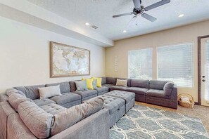 Ein Wohnzimmer mit Ecksofa, Deckenventilator und einer großen Weltkarte an der Wand.