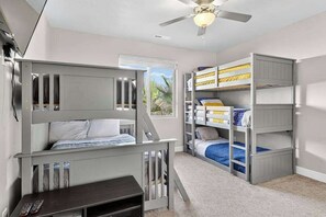 Une chambre d’enfant avec des lits superposés, un bureau et un ventilateur de plafond.