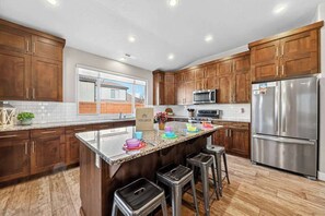 A modern kitchen with wooden cabinets, stainless steel appliances, and a central island with stools. - 5BR home with waterpark, private pool and spa (Santa Clara)