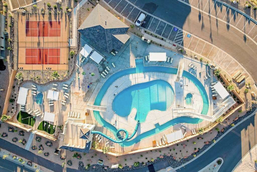 An aerial view of a resort with a large swimming pool, tennis courts, and a parking area.