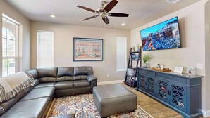 A living room with a sectional sofa, ottoman, ceiling fan, wall-mounted TV, and a patterned rug. - 5BR shared pool with slide near outdoors (Washington)