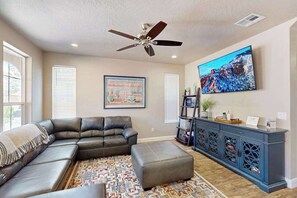 A living room with a sectional sofa, ottoman, ceiling fan, wall-mounted TV, and a patterned rug. - 5BR shared pool with slide near outdoors (Washington)