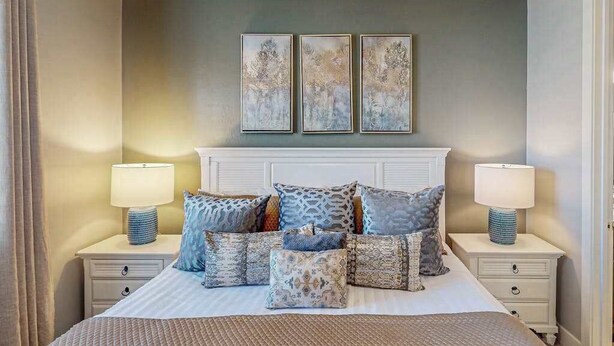 Quarto com cama, mesas de cabeceira, luminárias e três quadros na parede.
