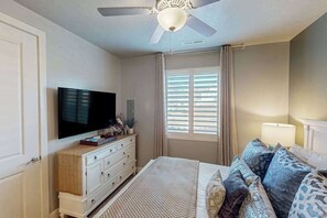 Een slaapkamer met een bed, een televisie, een plafondventilator en een raam met zonwering.