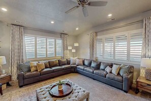 A living room with a large L-shaped sectional sofa, a round ottoman, and a ceiling fan. - 5 BR home with hot tub & water park PV90 (Santa Clara)