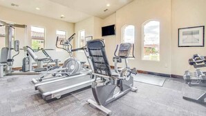 Uma academia com equipamentos de cardio, bancos de peso e uma televisão na parede.