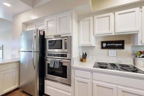 A modern kitchen with white cabinetry, stainless steel appliances, and a black and white sign on the wall.