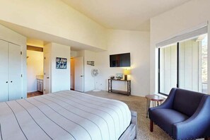A hotel room with a large bed, a blue armchair, a TV mounted on the wall, and a sign that reads 'GO JUMP IN THE LAKE'.