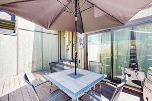 An outdoor patio with a table and chairs, a large umbrella, and a glass door leading to a deck.