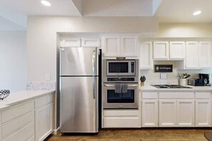 A kitchen with white cabinets, a stainless steel refrigerator, a microwave, and an oven.
