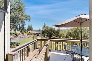 A deck with a table and chairs, a large umbrella, and a view of a road and trees.