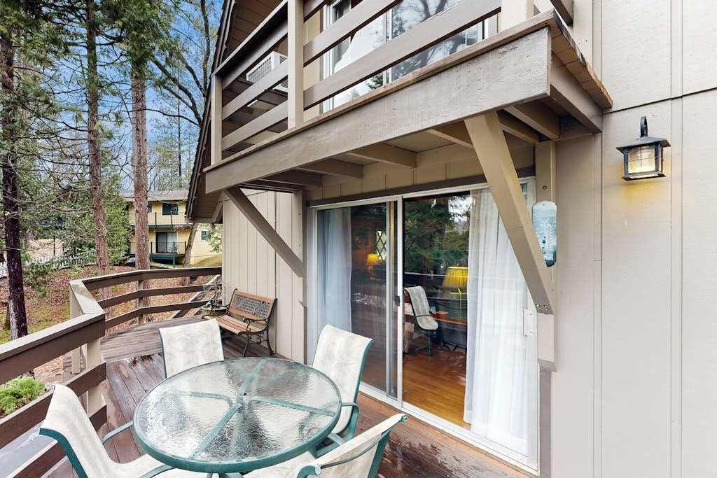 Une terrasse en bois avec une table et des chaises en verre, un banc et une vue sur une zone boisée.