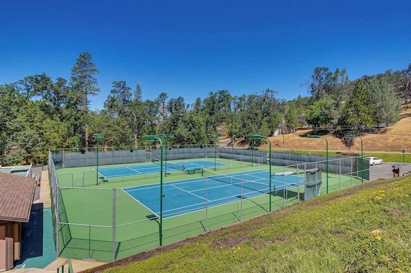 A tennis court with multiple courts, surrounded by a fence, and trees in the background.