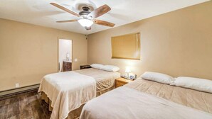 Ein Hotelzimmer mit zwei Betten, einem Deckenventilator, einem Nachttisch mit Lampe und einem Fenster mit Jalousien.