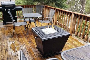 A deck with a grill, a table with chairs, and a fire pit. - Tamarack Dream - Tamarack Estates (Lakeshore)