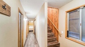 Ein enger Flur mit Holzboden, eine Treppe mit Holzwangen und einem Geländer, und ein großes Fenster auf der rechten Seite.