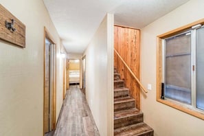 Ein enger Flur mit Holzboden, eine Treppe mit Holzwangen und einem Geländer, und ein großes Fenster auf der rechten Seite.