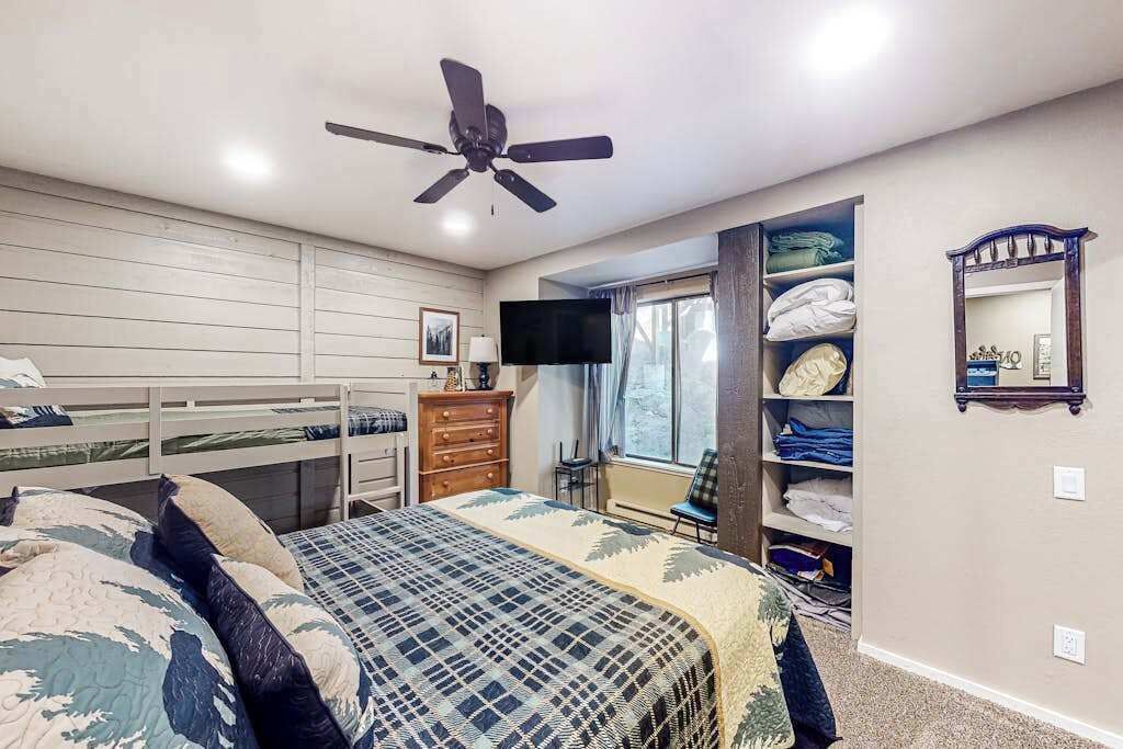Ein Schlafzimmer mit Etagenbetten, Deckenventilator, Fernseher, einem Fenster mit Vorhängen und einem Kleiderschrank.