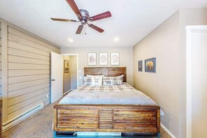 A bedroom with a wooden bed, a ceiling fan, and framed artwork on the walls.
