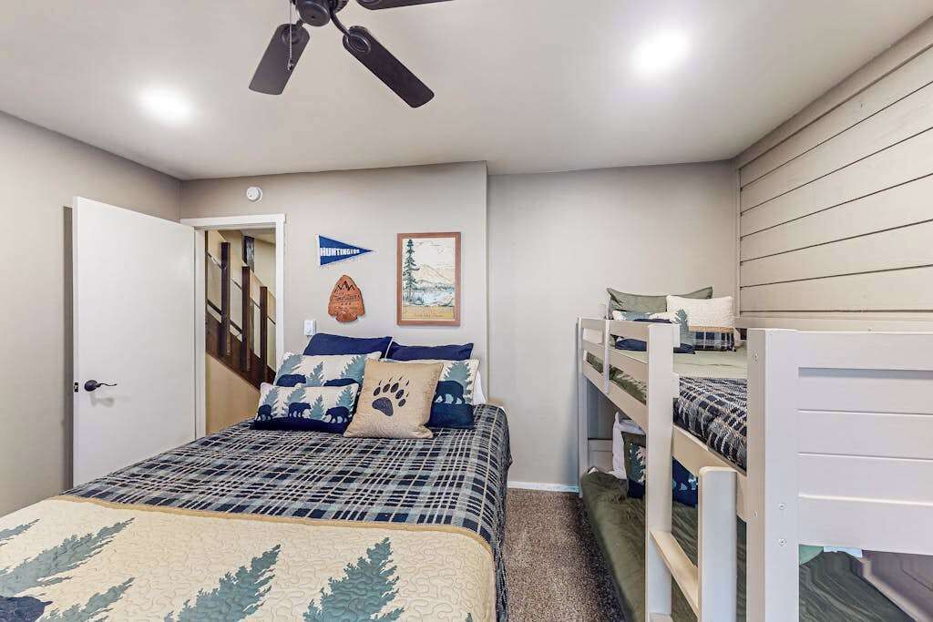 A bedroom with a bed, bunk beds, a ceiling fan, and a door leading to a staircase.