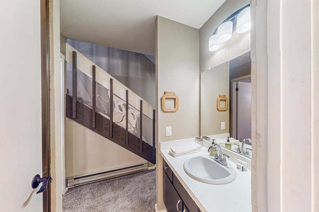 Une salle de bain avec un lavabo blanc, un miroir et un escalier menant à une autre pièce.